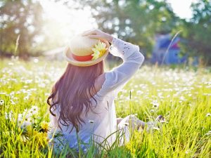 Woman with sun hat on, sitting in a grassy meadow, looking at the full-spectrum light of the sun.